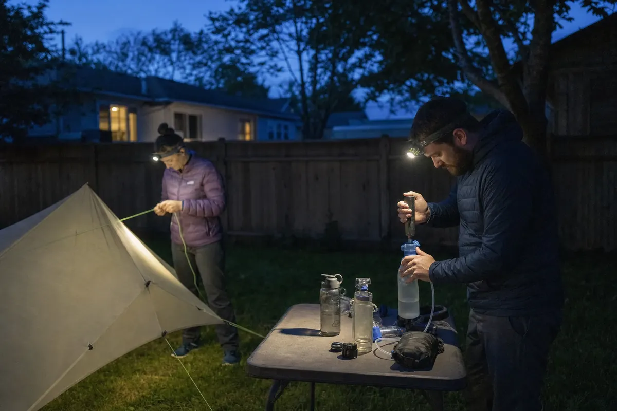 Beginner backpackers practicing tent setup and water treatment under headlamps near home - low-light backpacking practice | KnowOutdoor