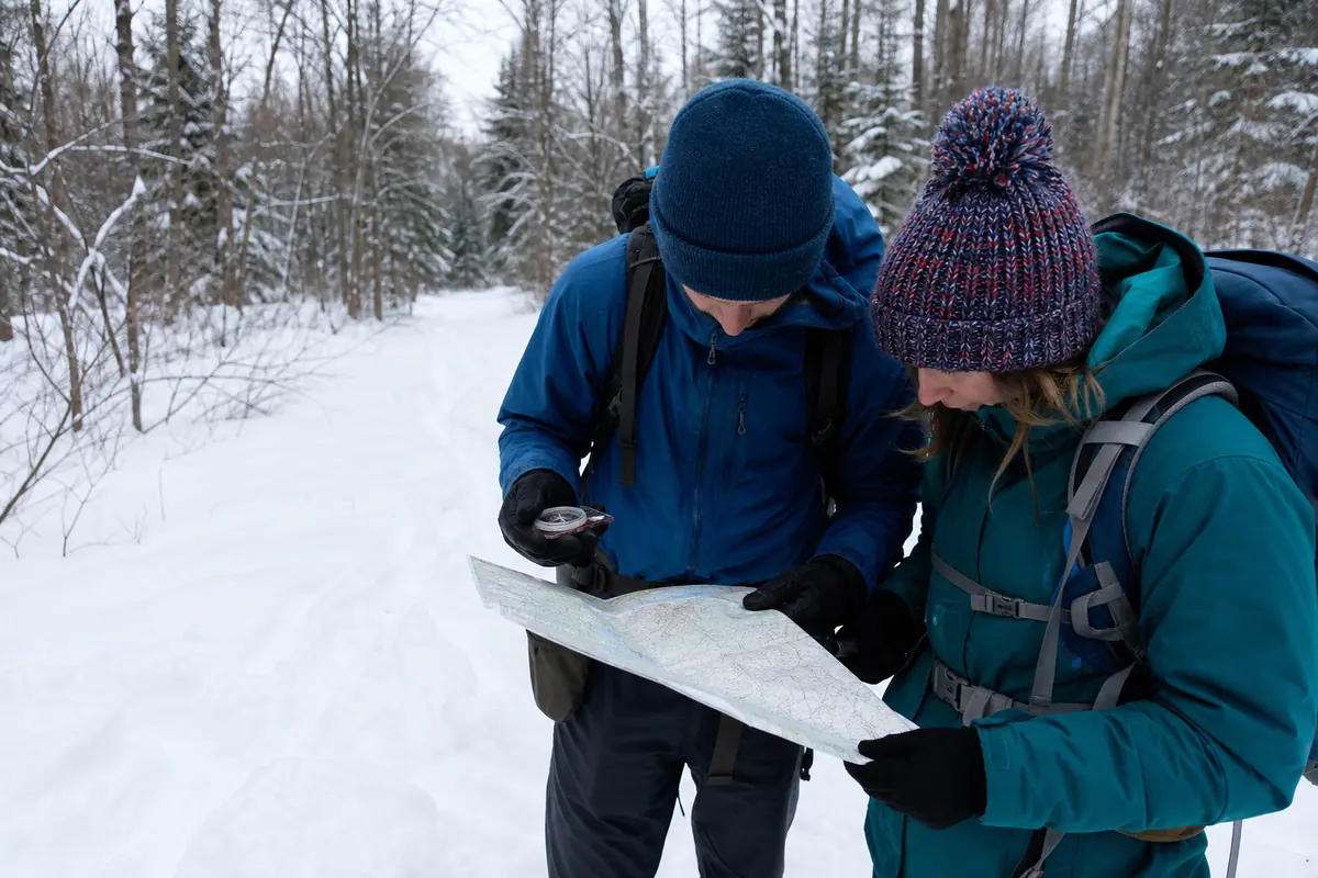 Winter backpackers using a paper map and compass where snow has covered a generic trail junction and previous tracks diverge - winter backpacking navigation | KnowOutdoor