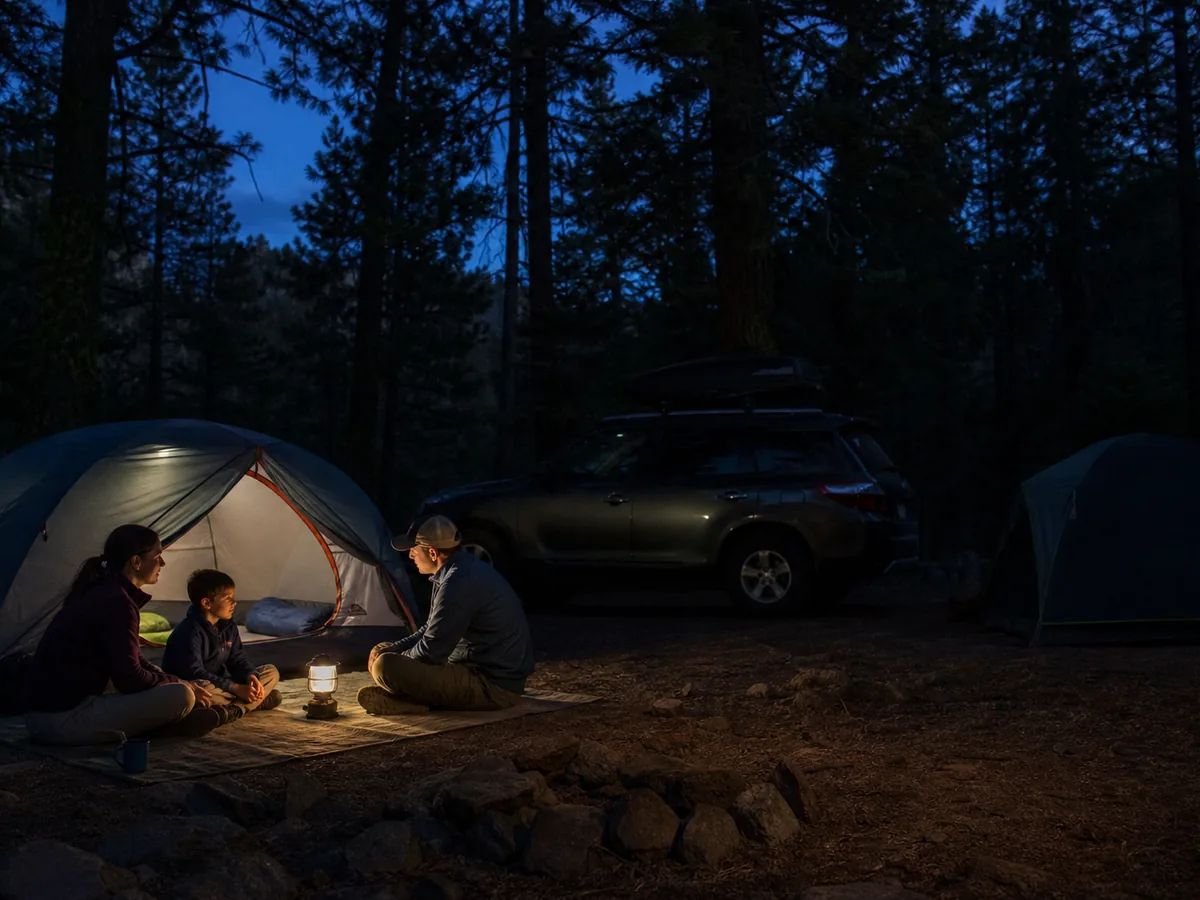 Family using one low shielded lantern inside their campsite while neighboring tents remain dark - quiet campground lighting | KnowOutdoor