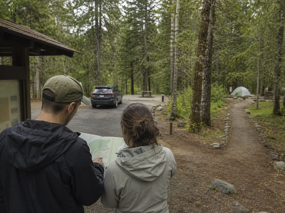 Campers comparing a drive-in parking spur and marked walk-in campsite path on a campground map - campground site types | KnowOutdoor