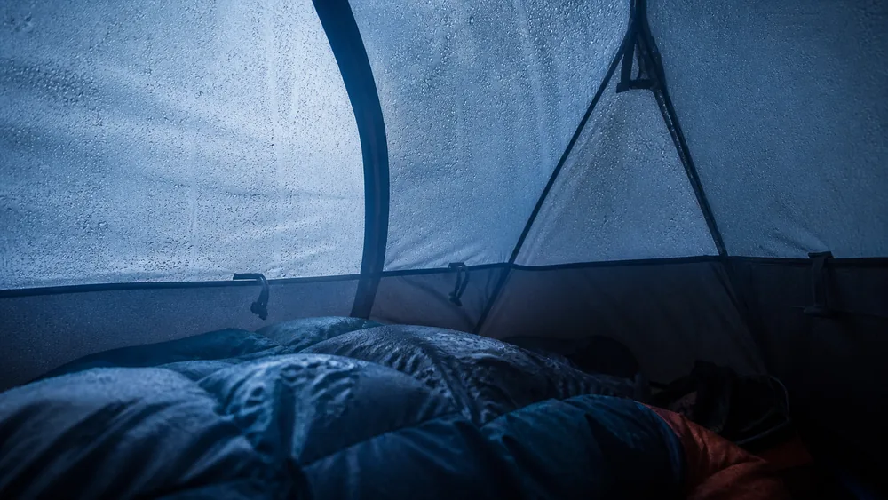Inside a small tent at dawn with heavy condensation beaded across the inner fabric and dampness on the top of a sleeping bag | KnowOutdoor