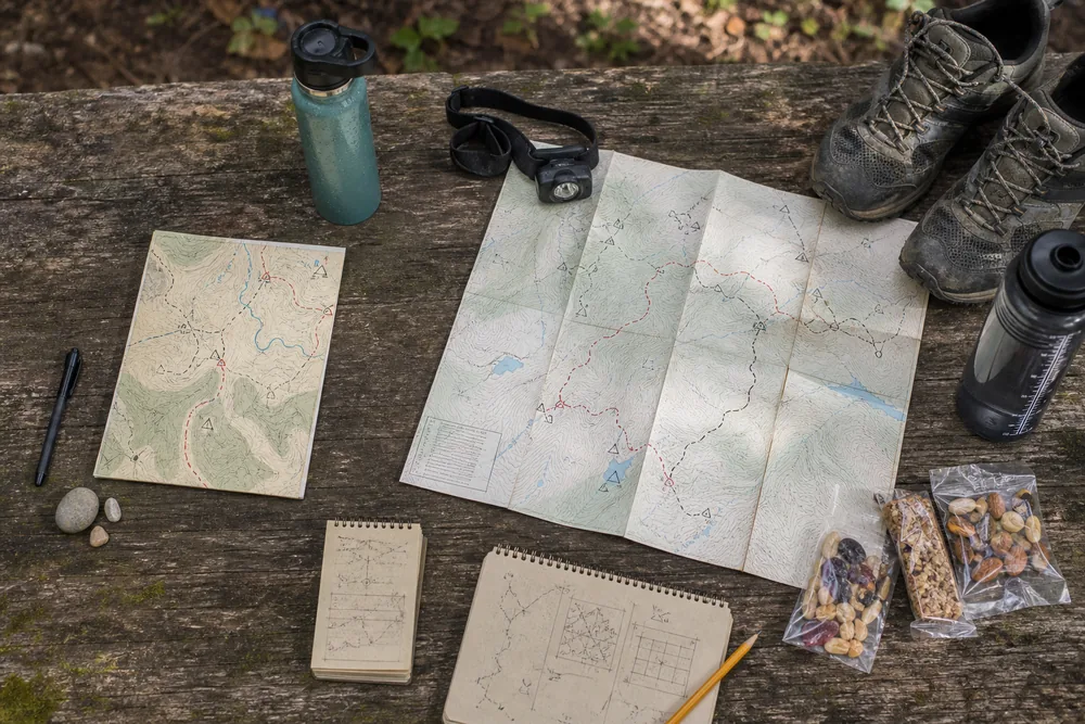 Single-day hiking note beside multi-day trekking route plan and trail gear