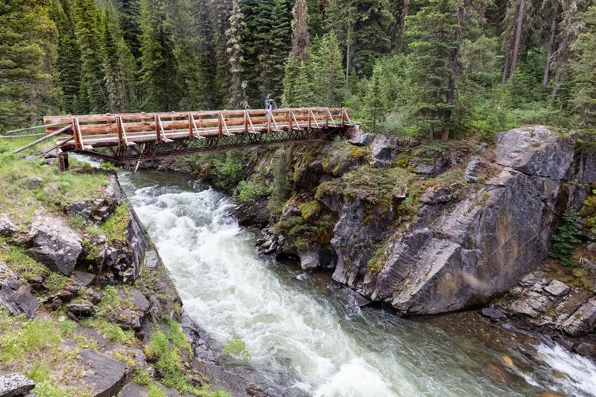 Backpacker crossing Hellroaring Creek on a wilderness bridge - Absaroka-Beartooth Wilderness | KnowOutdoor