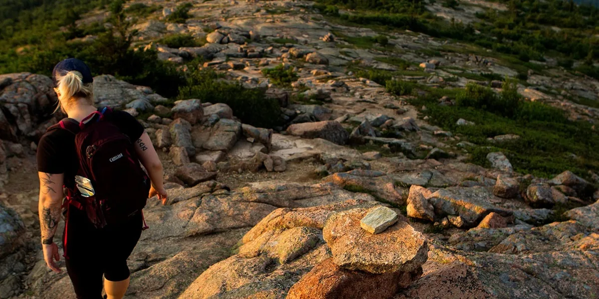 Hiker descending a cairn-marked granite ridge on Cadillac Mountain in Acadia National Park - Acadia National Park | KnowOutdoor