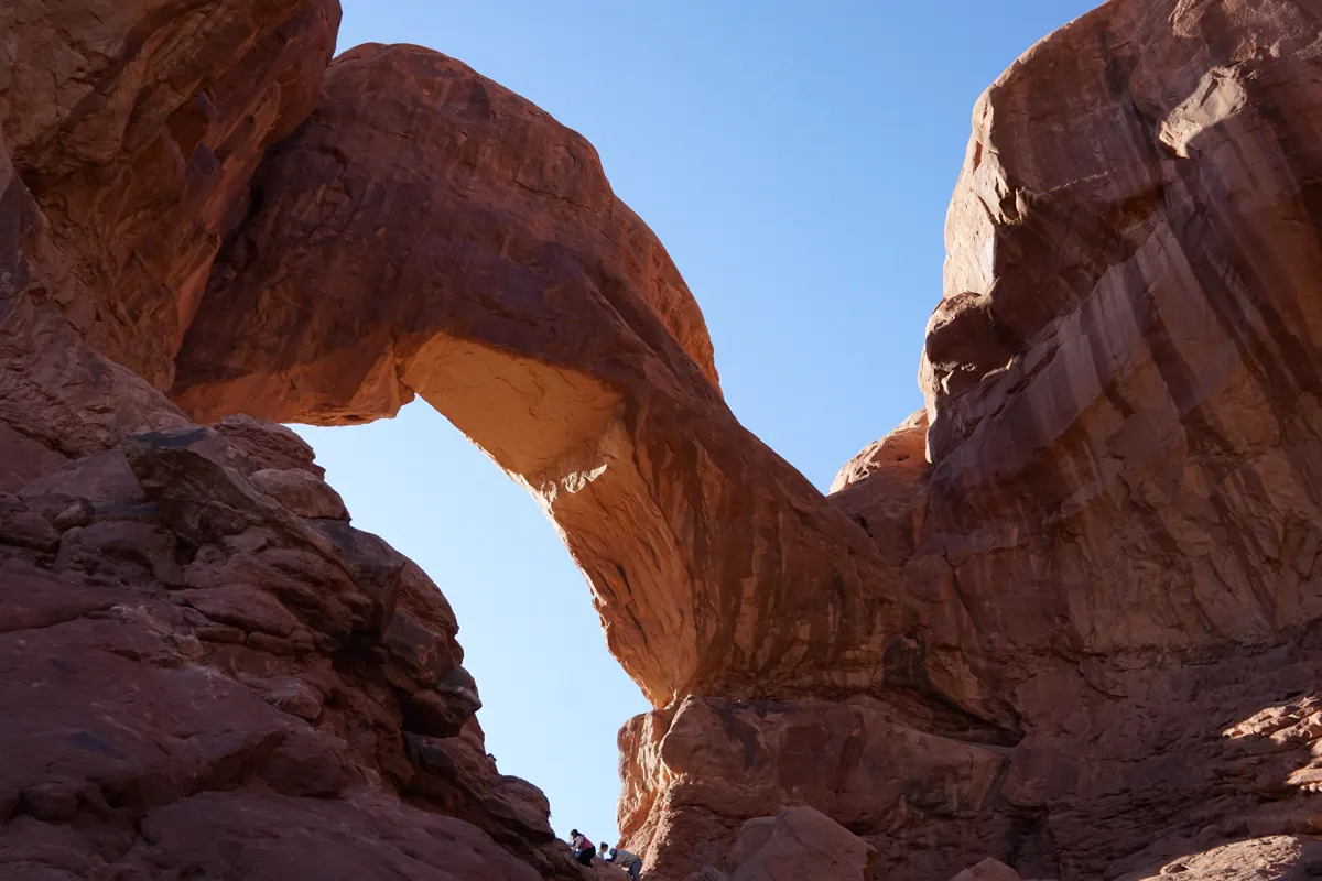 Visitors scrambling on sandstone beneath an arch at Arches National Park