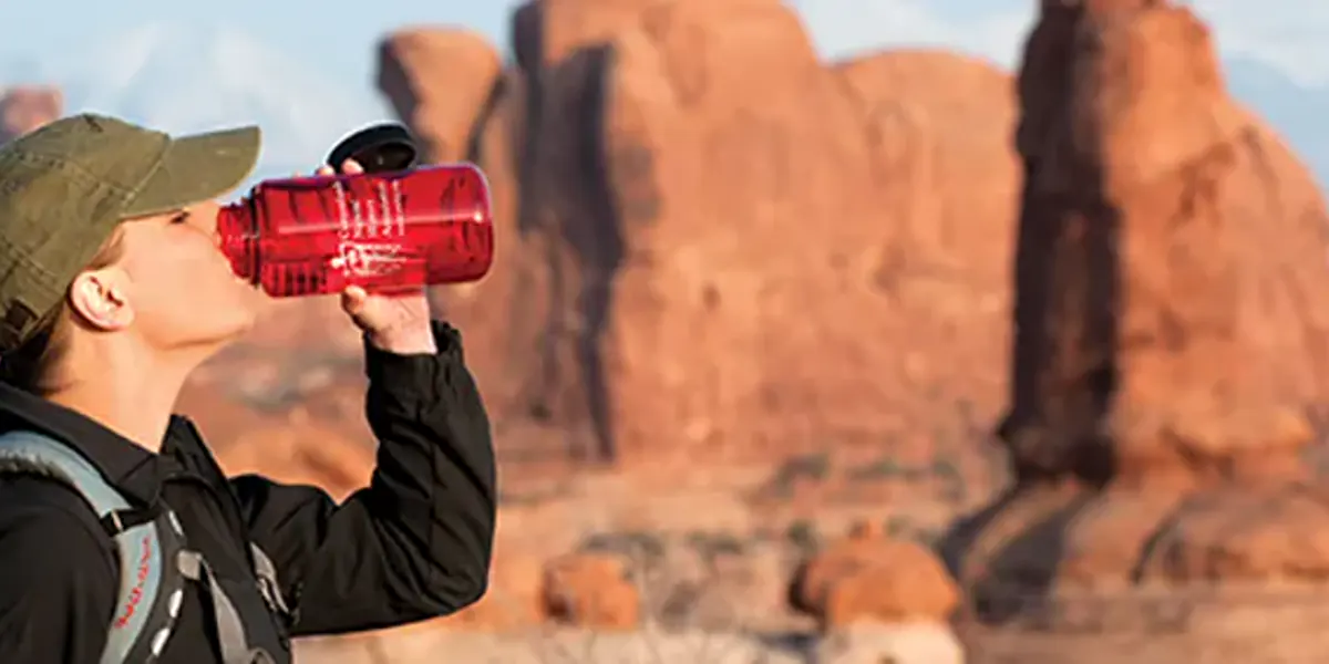 Hiker drinking water in exposed red rock terrain at Arches National Park
