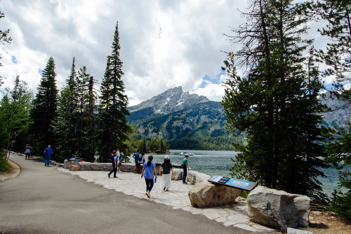 Visitors walking a paved lakeshore path beside mountains in Grand Teton National Park