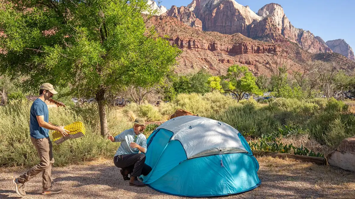 Two campers pitching a blue tent below Zion Canyon cliffs - Zion National Park | KnowOutdoor