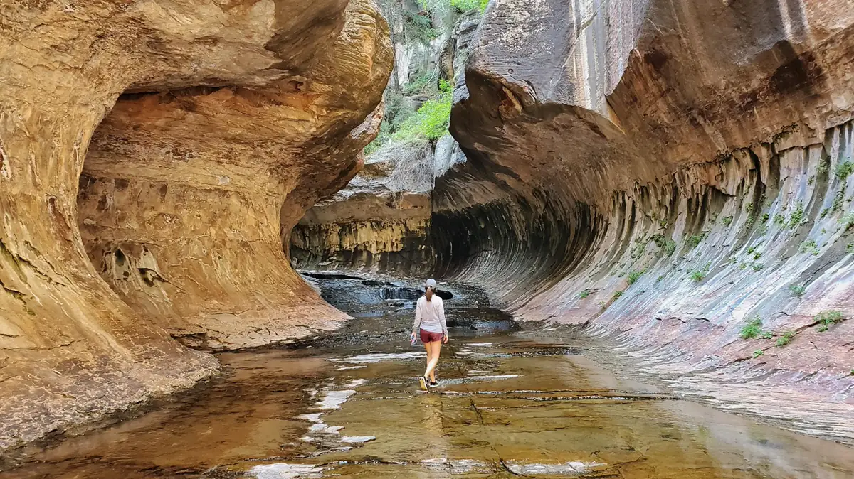 Hiker walking through a confined creek between curved sandstone walls - Zion National Park | KnowOutdoor