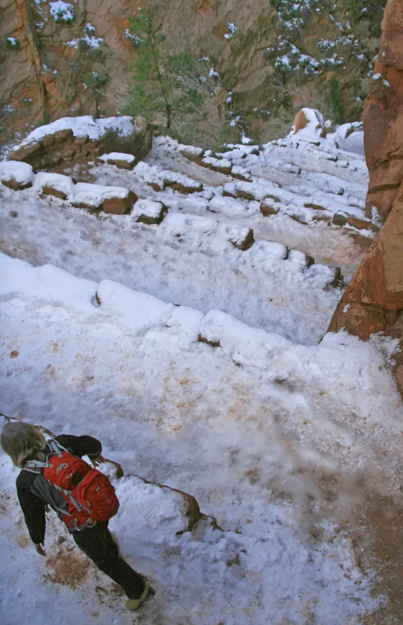 Hiker descending snow-covered switchbacks between red sandstone walls - Zion National Park | KnowOutdoor