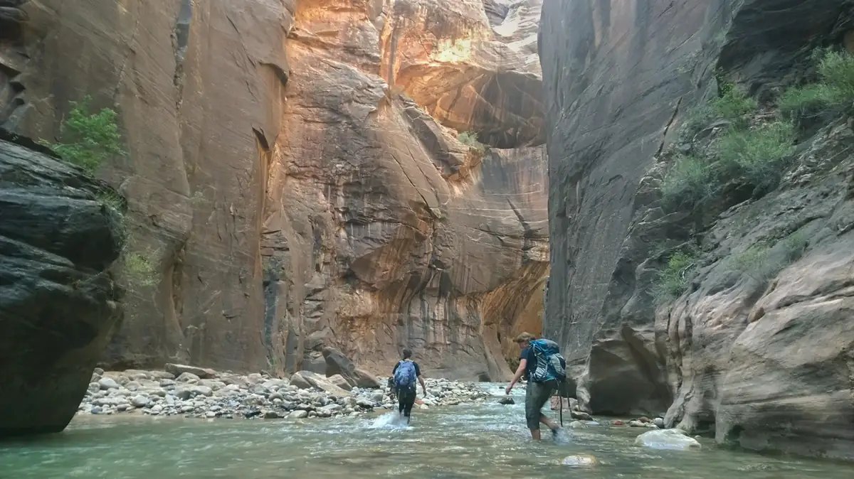 Two hikers wading between tall sandstone walls in the Narrows - Zion National Park | KnowOutdoor