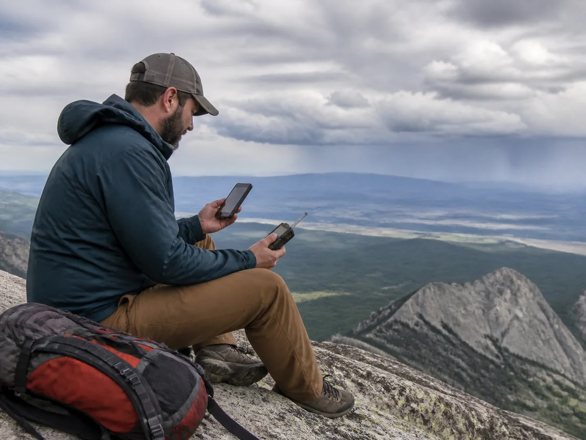 Hiker using a generic compact satellite communicator paired with a phone on an open trail - phone-based satellite messaging | KnowOutdoor