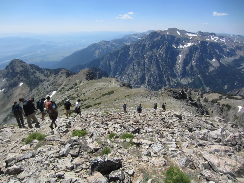 Hikers descend a rocky alpine ridge above steep mountain valleys - Grand Teton National Park | KnowOutdoor