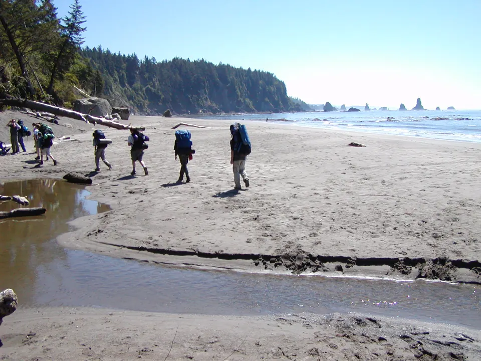 Backpackers cross a wild Pacific beach lined with sea stacks - Olympic National Park | KnowOutdoor