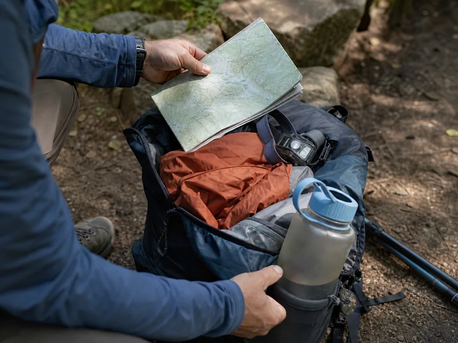 Day hiker checking map, water, shell, and headlamp before starting