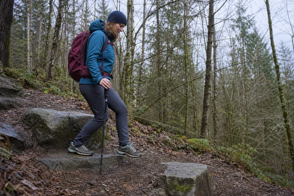 Hiker practicing a slow controlled step-down from a low stone step on an easy forest path