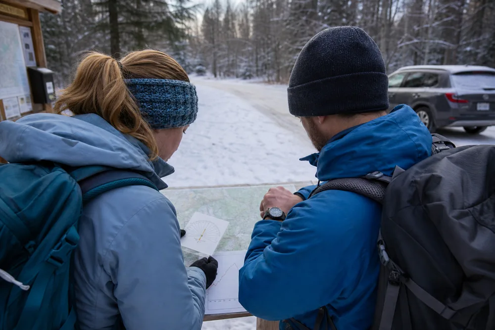 Winter hikers calculating a turnaround time from trailhead finish, snowy return pace, delay buffer, and late access
