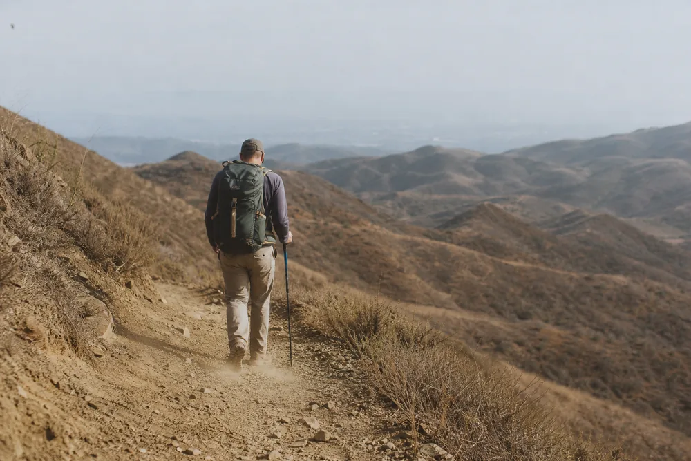 Hiker walking downhill on an open dusty trail under hazy sky - exiting toward the trailhead | KnowOutdoor
