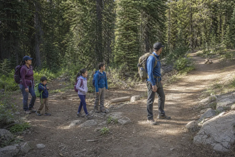Two adults keeping a small family hiking group together with one adult leading near a junction and another staying behind the slowest child