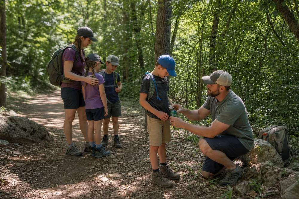 Family stopped in shade while an adult checks a child's water, temperature, speech, gait, shoes, and comfort before deciding to turn around
