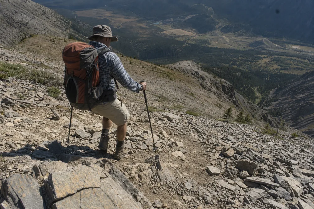Hiker descending a steep rocky trail section late in the day with tired posture - choosing a day hike for your fitness | KnowOutdoor