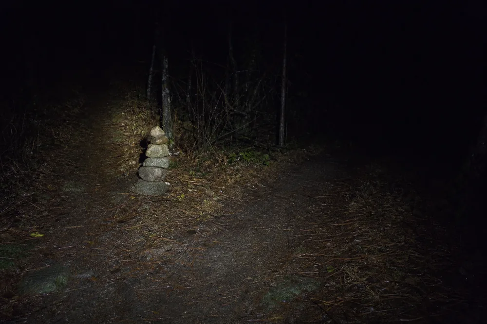 Unsigned trail fork at night lit only by a headlamp beam with a small cairn marking the left branch - sunrise and sunset hiking | KnowOutdoor