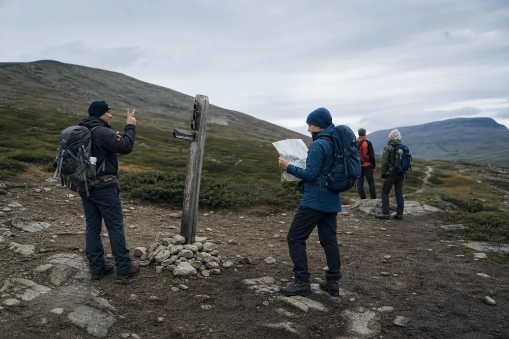Hikers paused at a wooden trail junction post counting heads while one checks a paper map - group hiking headcount | KnowOutdoor