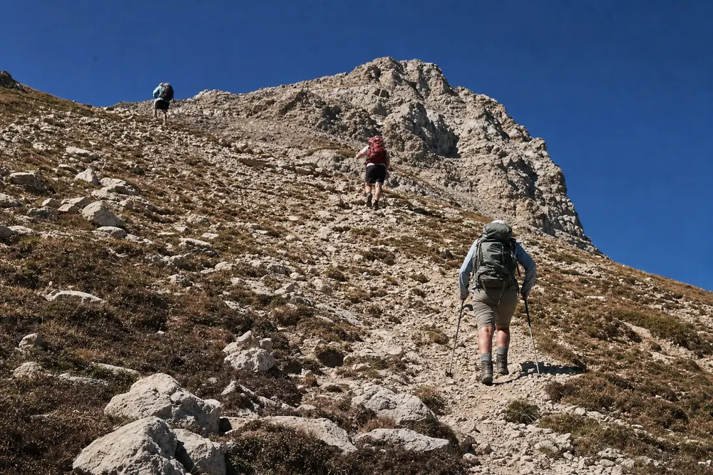 Three hikers spread several body lengths apart while climbing a steep loose rocky trail toward a saddle - group hiking spacing | KnowOutdoor
