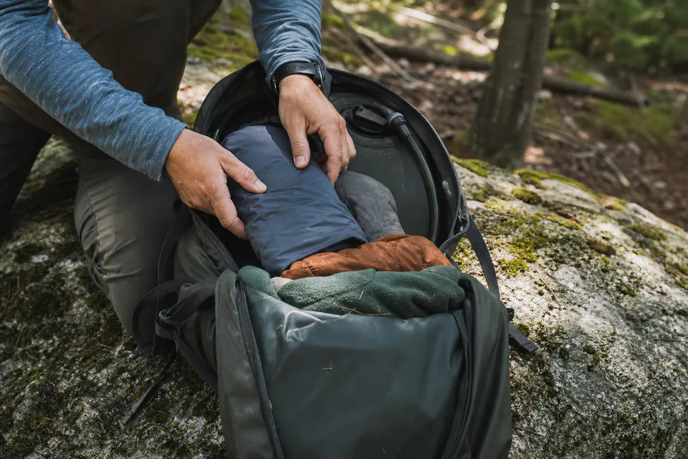 An open daypack on a boulder showing dense items packed against the back panel with soft clothing filling the outer space - daypack load placement | KnowOutdoor