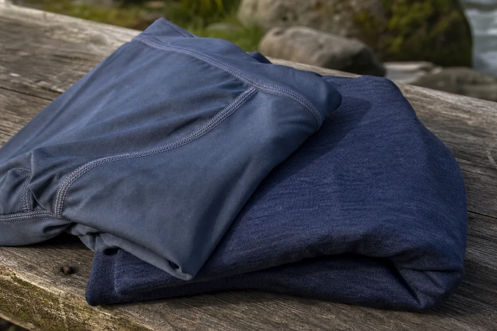 Folded hiking shorts and merino base layer on a wooden bench showing flat-lock seam stitching - hiking chafing prevention | KnowOutdoor