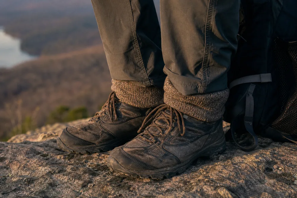Seated hiker's trail shoes and tall wool socks with the cuff turned down over the shoe collar on a dusty trail rock - hiking chafing prevention | KnowOutdoor