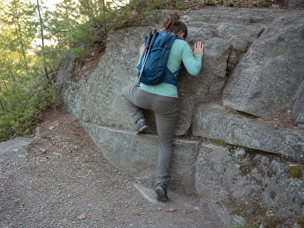 Hiker facing low rock while lowering one boot toward a broad visible foothold
