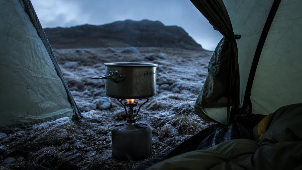 Camp stove burning under an open tent vestibule with the fly rolled back on a cold high camp - carbon monoxide risk mistaken for altitude sickness | KnowOutdoor