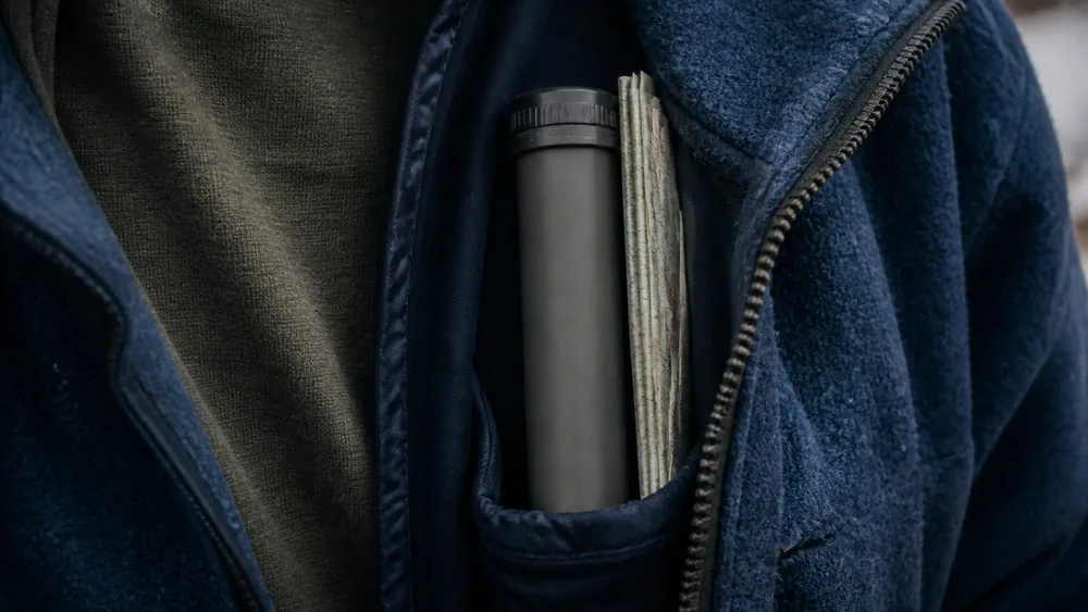 An auto-injector in its protective carrier tube tucked inside a jacket chest pocket next to a folded map on a cold day - field storage of epinephrine | KnowOutdoor
