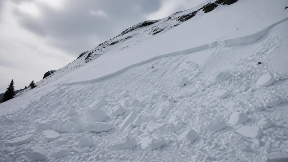 Fresh avalanche debris of broken hard snow blocks piled at the base of a slope with a clean fracture line visible higher up - the clearest warning sign available to an untrained party | KnowOutdoor