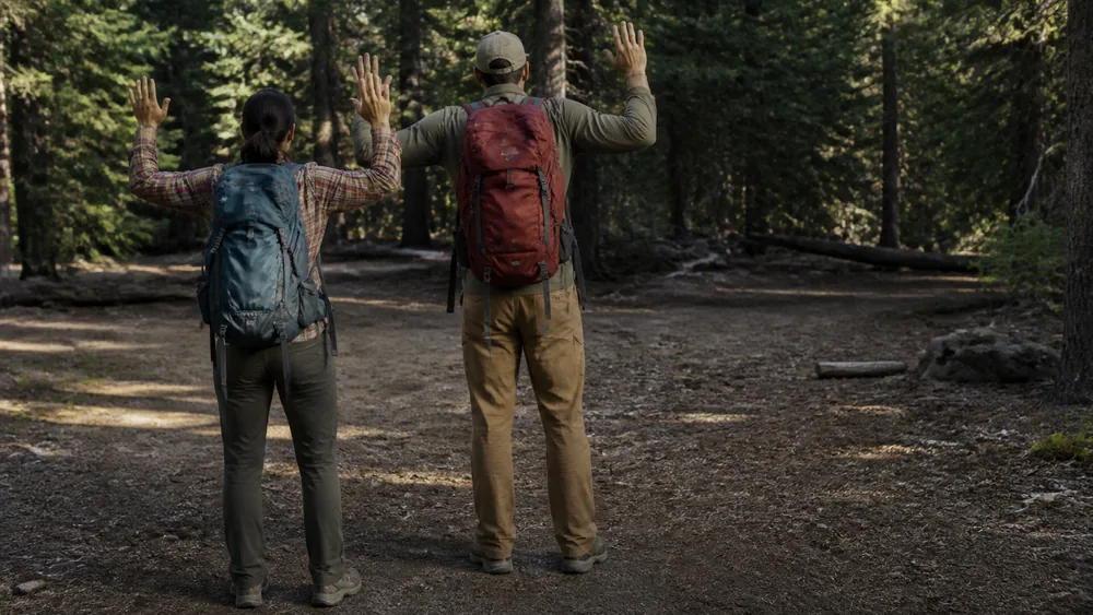 Two hikers standing close together on a trail seen from behind with arms raised slowly and slightly out, calm posture, facing open ground - the retreat behaviour during a bear encounter | KnowOutdoor