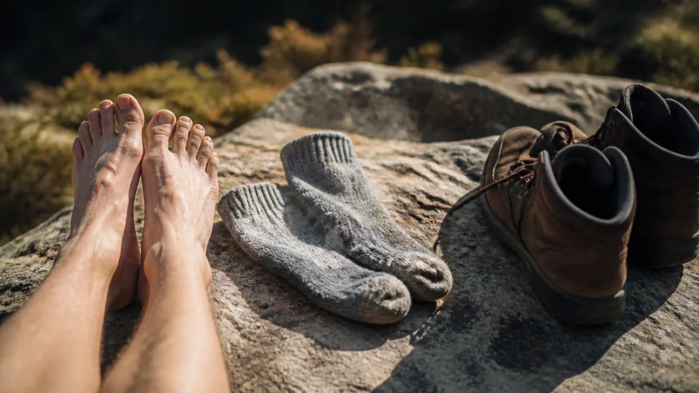 Bare feet and damp wool socks laid over a warm rock at a trail rest stop with boots open beside them | KnowOutdoor