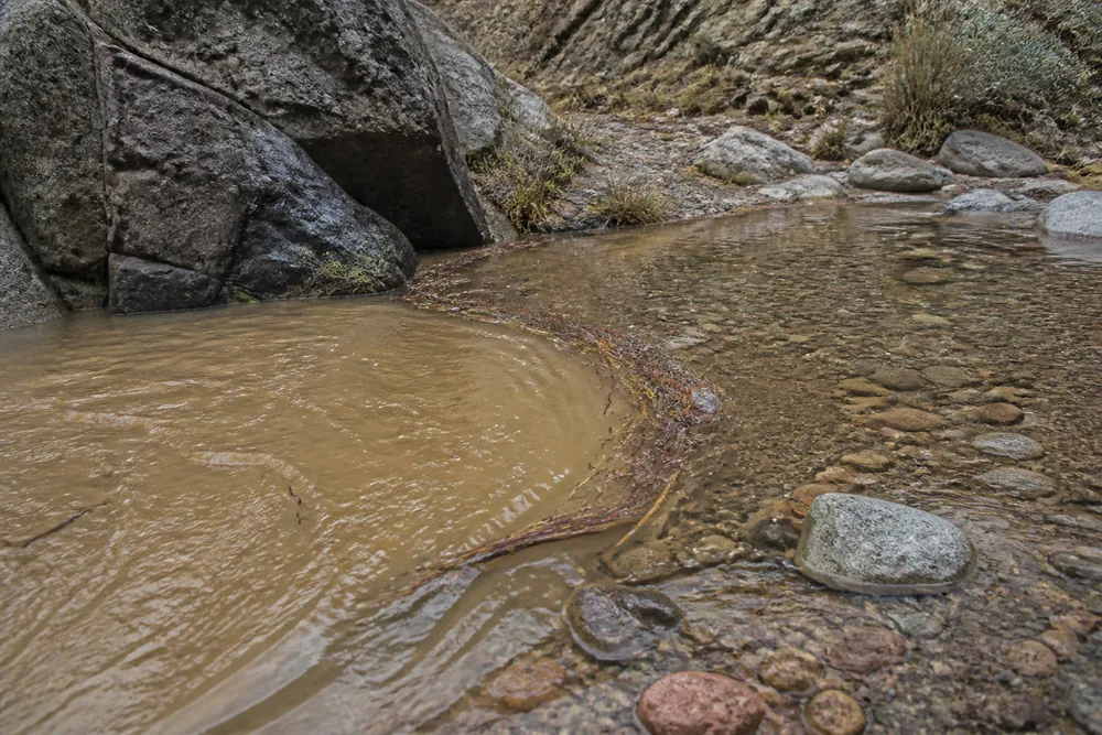 Brown sediment-laden water pushing into a clear shallow pool at a bend in a rocky canyon | KnowOutdoor