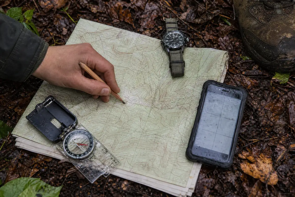 Topographic map, compass, watch, pencil and phone beside a stationary hiking boot on a damp forest trail - getting lost location record | KnowOutdoor