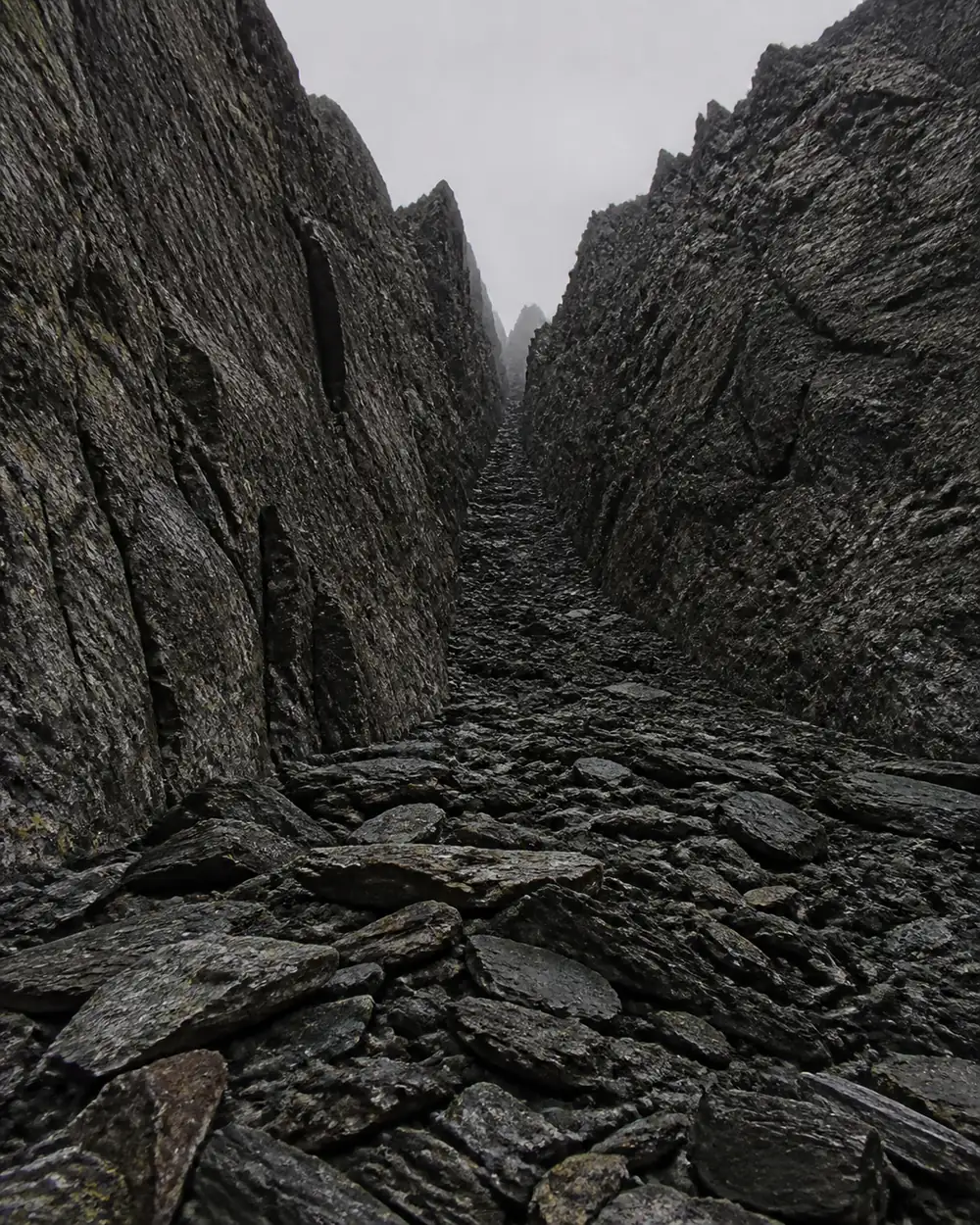Looking straight up the axis of a narrow alpine couloir from the scree fan at its base, rock walls closing in on both sides with no line out to either flank - the geometry that aims falling rock at the route | KnowOutdoor