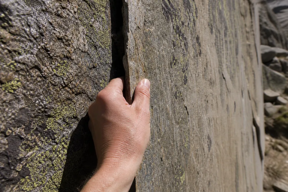 A hand testing a large thin rock flake on an alpine face with a continuous dark crack separating it from the rock behind - the detached block that looks solid until it is weighted | KnowOutdoor