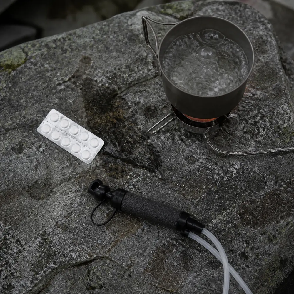 A rolling boil, purification tablets, and a portable squeeze filter arranged on rock - Backcountry water purification | KnowOutdoor