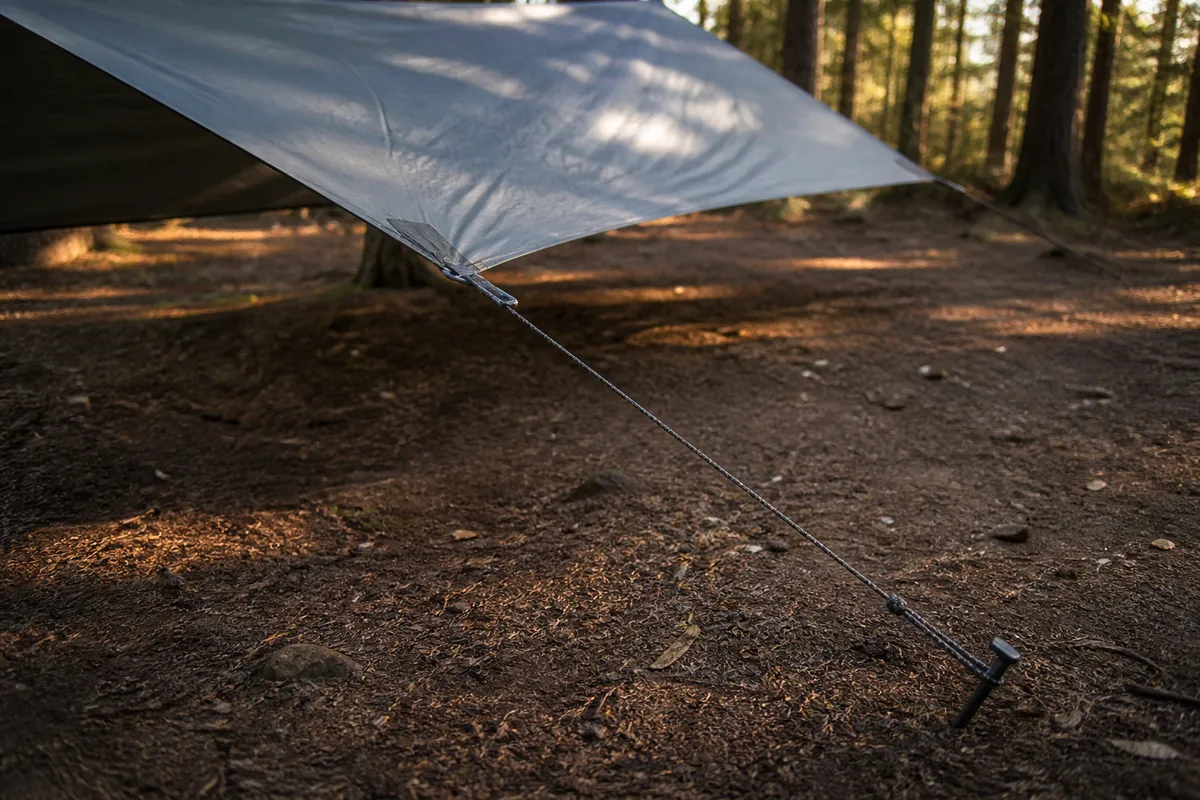 Ground-level view of a tarp corner guyline aligned with the reinforced tie-out and a correctly seated stake