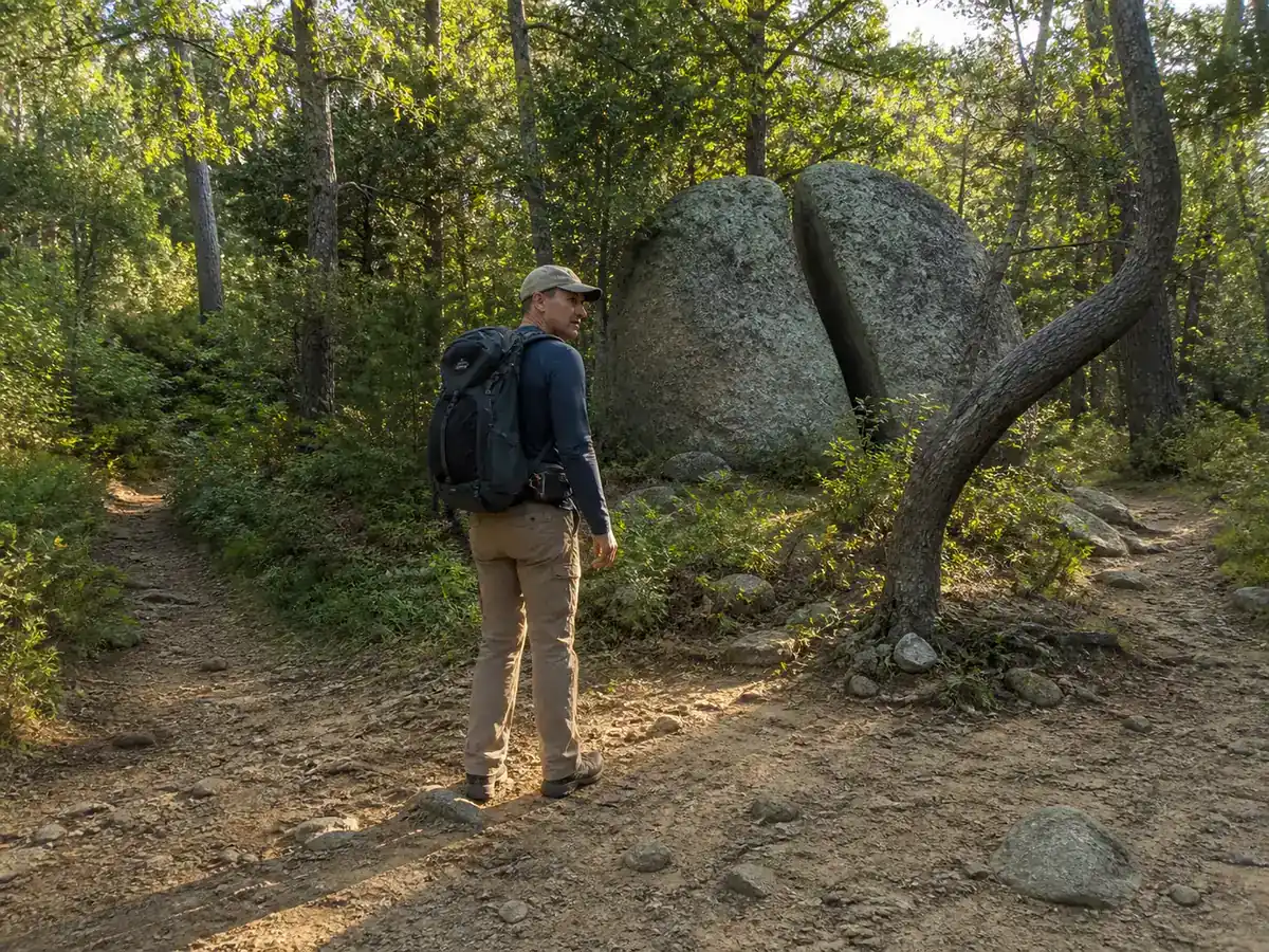 Hiker looking back at a split boulder and bent tree between two woodland paths - staying found at junctions | KnowOutdoor