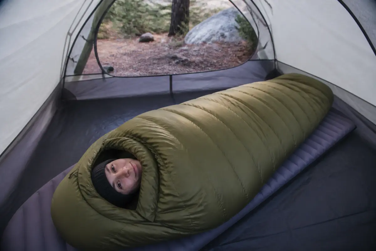 Sleeper in a correctly sized mummy bag with full loft, closed draft collar, shaped hood, relaxed footbox, and no heavy gear compressing the insulation