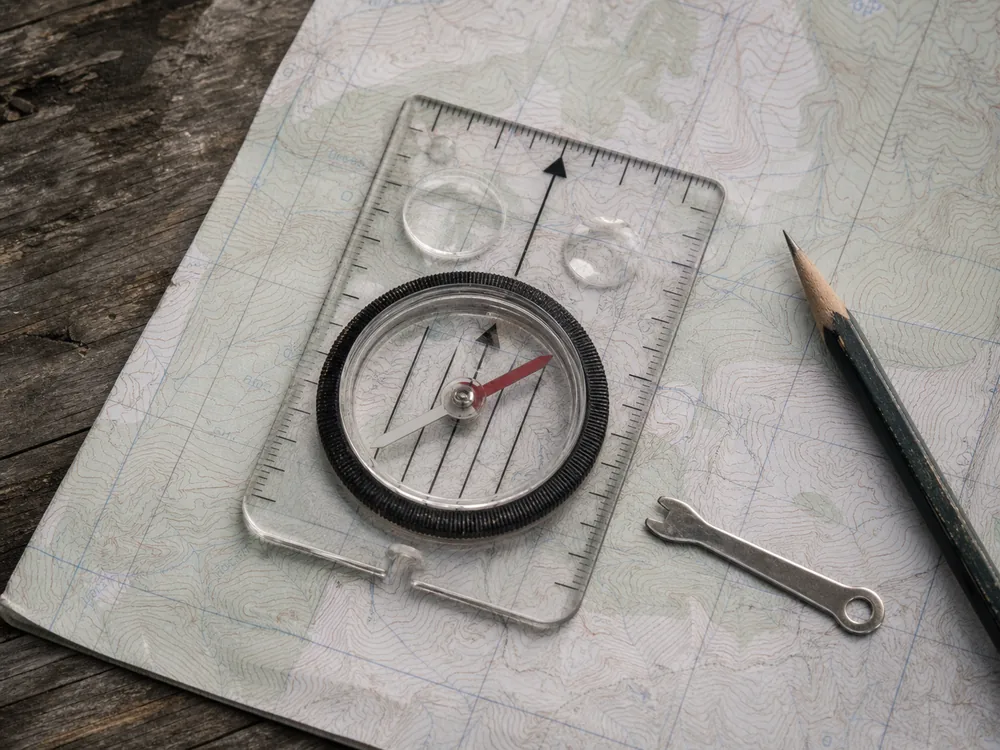 Adjustable baseplate compass, map, pencil, and declination key prepared on an outdoor table