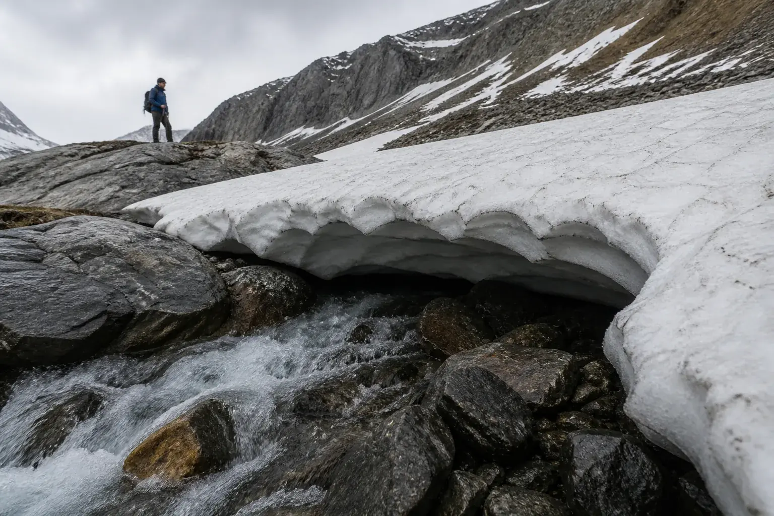 Collapsed edge of a generic alpine snow bridge exposing fast meltwater and a hollow gap over rocks