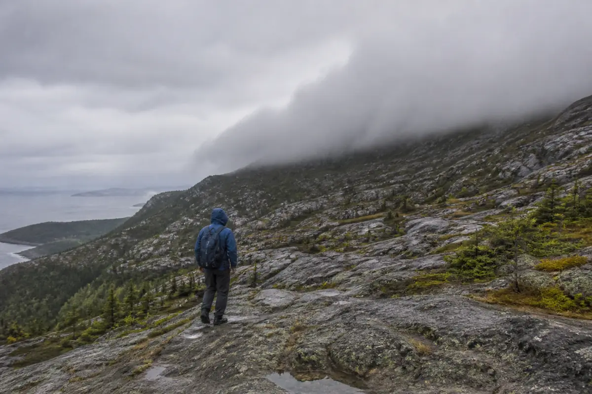 Generic alpine hiker stopped below a descending cloud ceiling while the lower return ridge remains visible