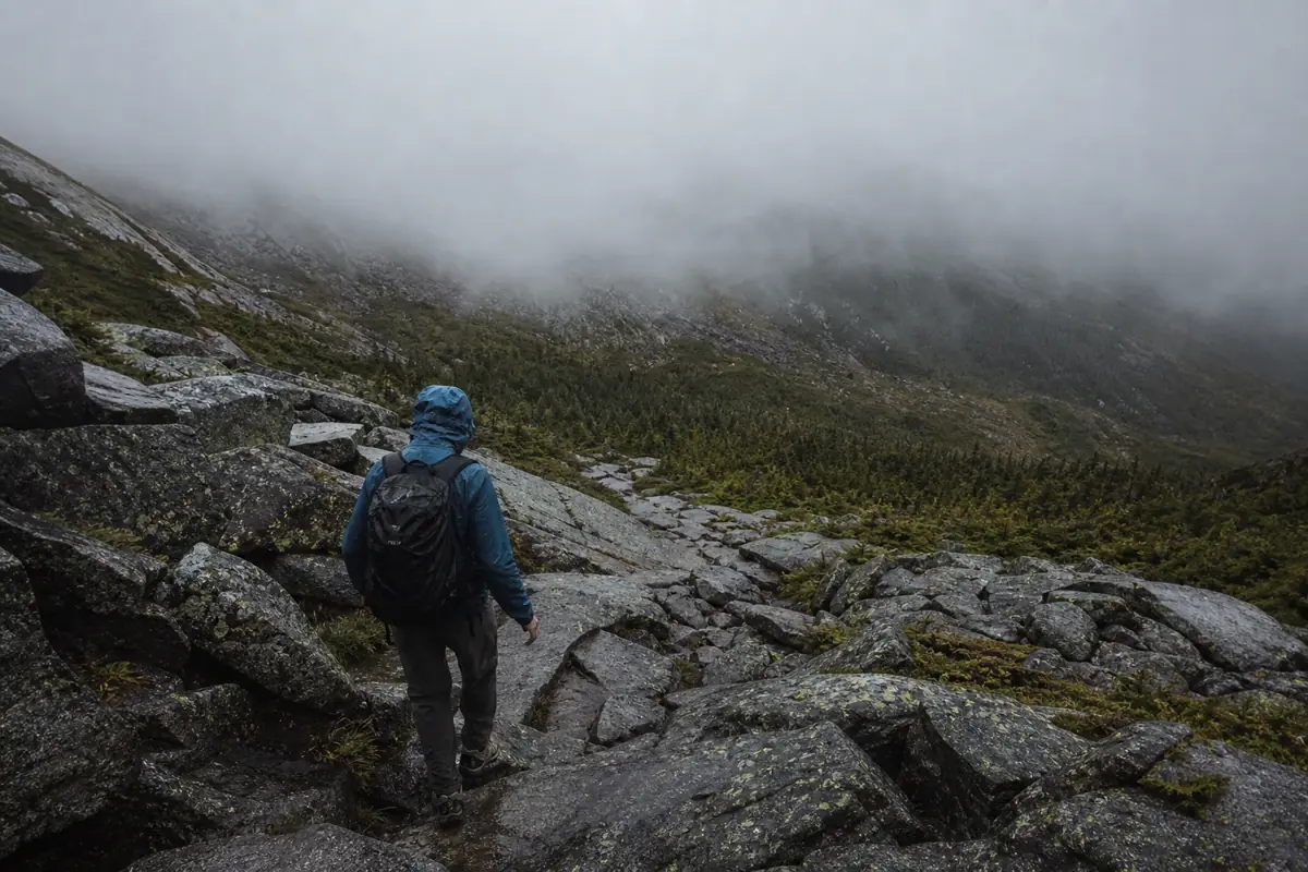 Generic hiker descending wet alpine boulders below low cloud on a northeastern mountain