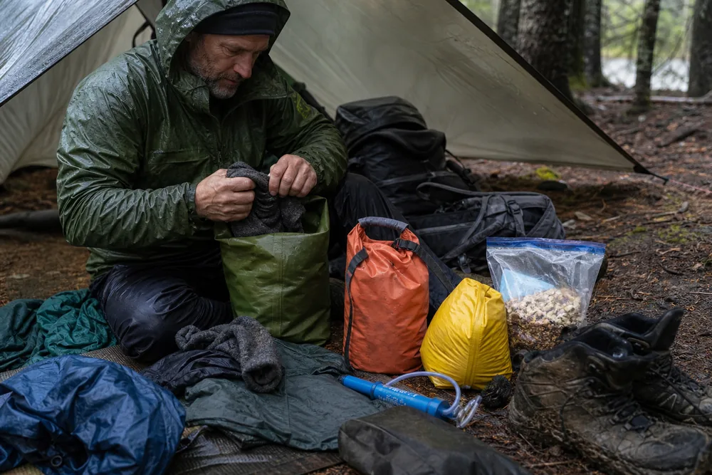 Trekking gear being repacked into dry bags under a tarp after rain